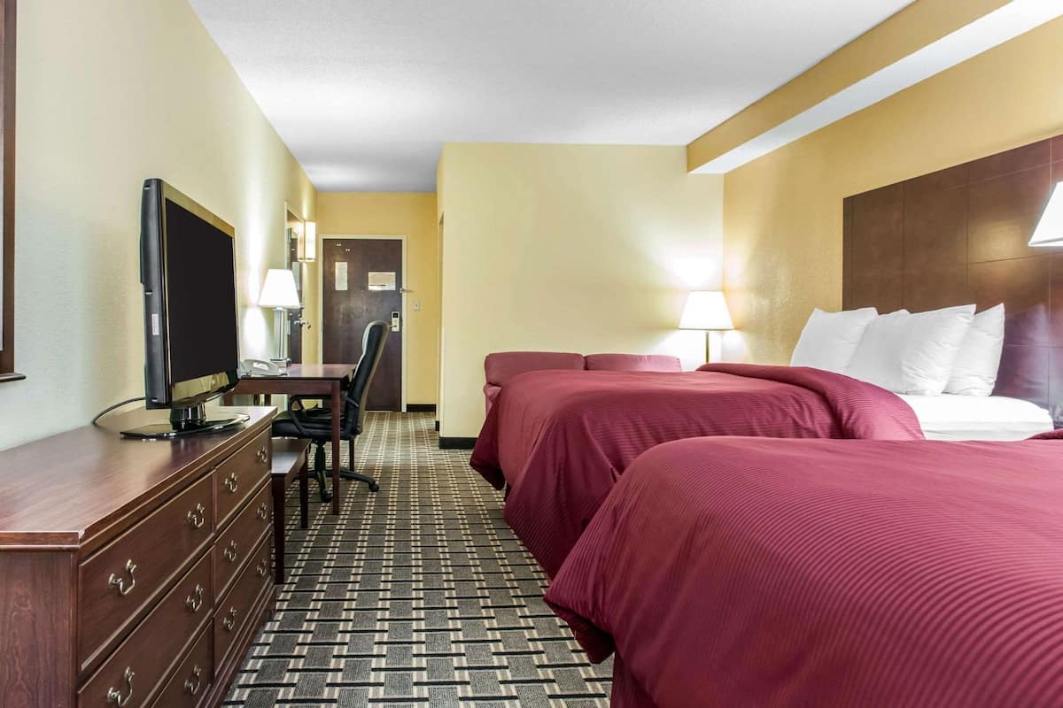A hotel room with a bed, a desk with a computer, a chair, and a television.