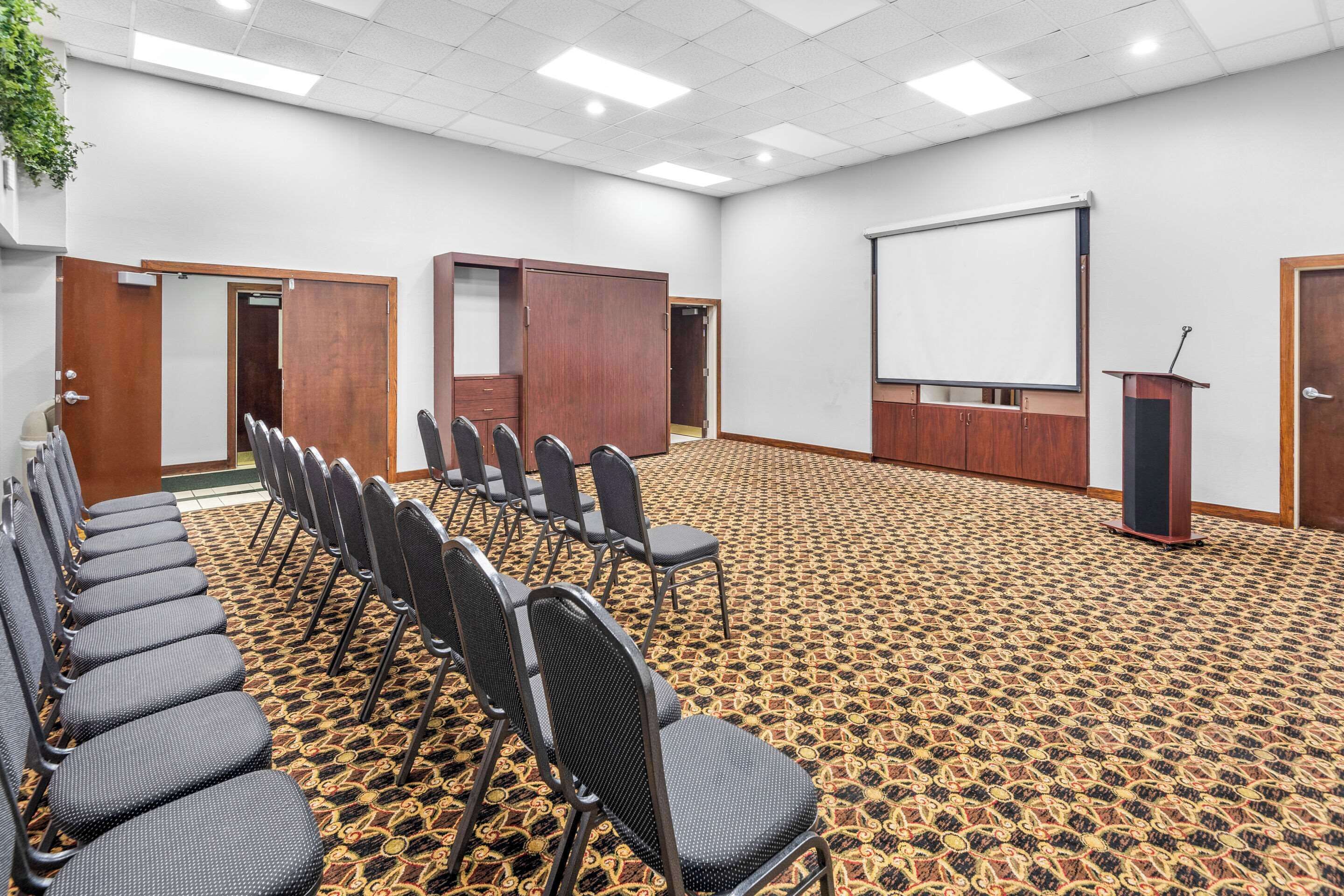A conference room with rows of chairs, a projector screen, and a podium.