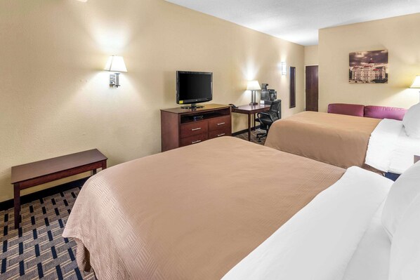 A hotel room with two beds, a desk, a television, and a lamp.