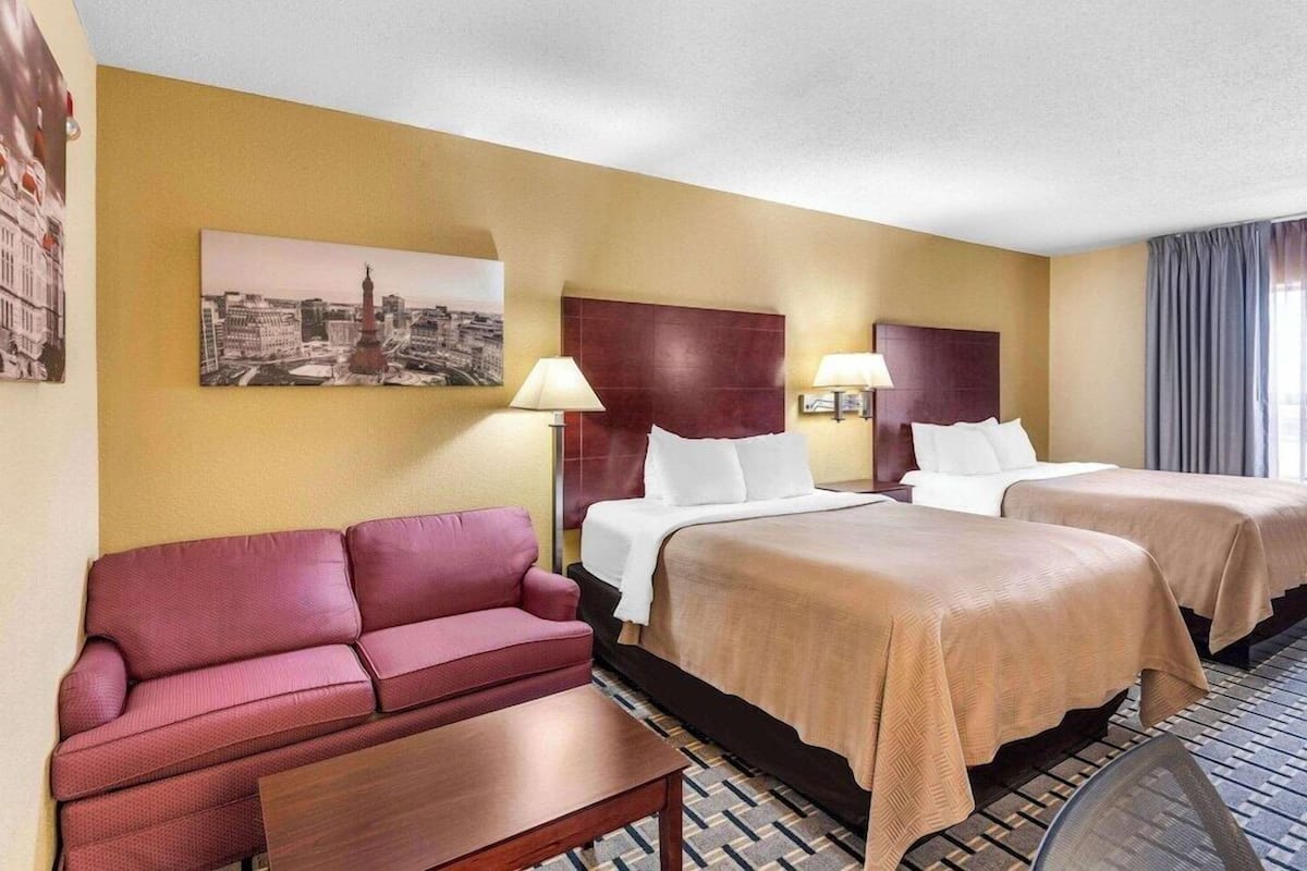 A hotel room with two beds, a sofa, and a table.