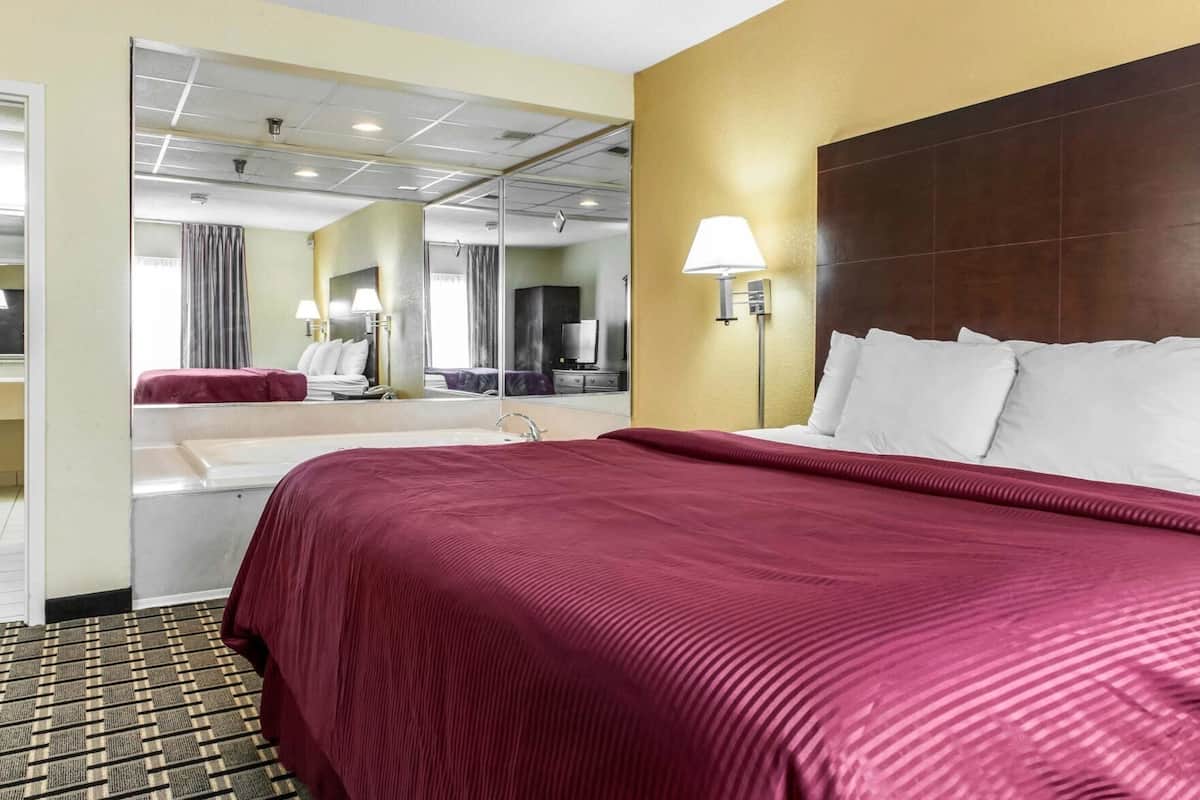 A hotel room with a large bed, a bathroom with a sink and mirror, and a view of the hallway.