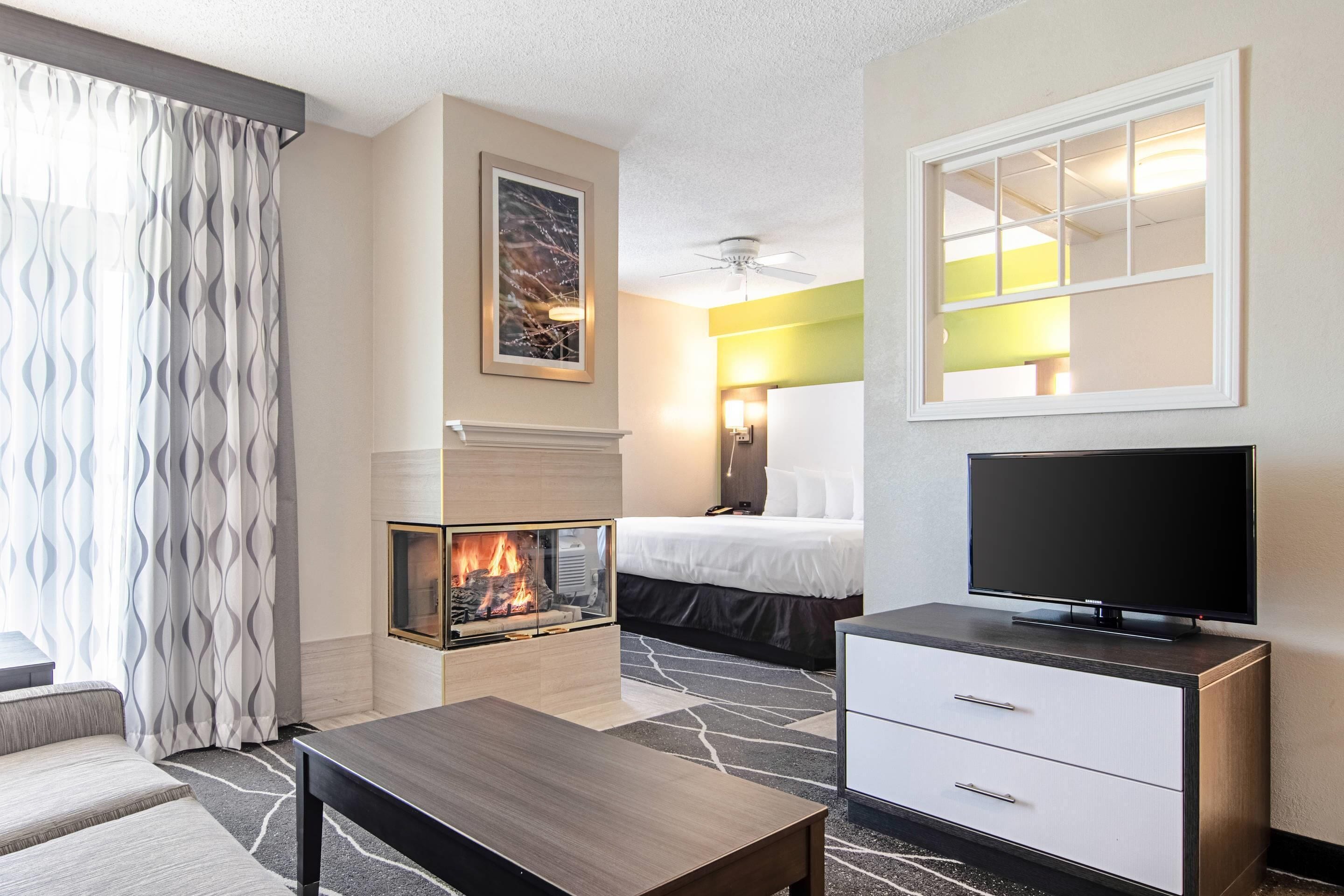 A hotel room with a fireplace, a bed, a television, and a desk.