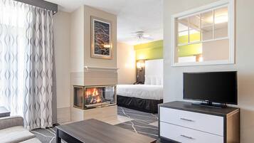 A hotel room with a fireplace, a bed, a television, and a desk.