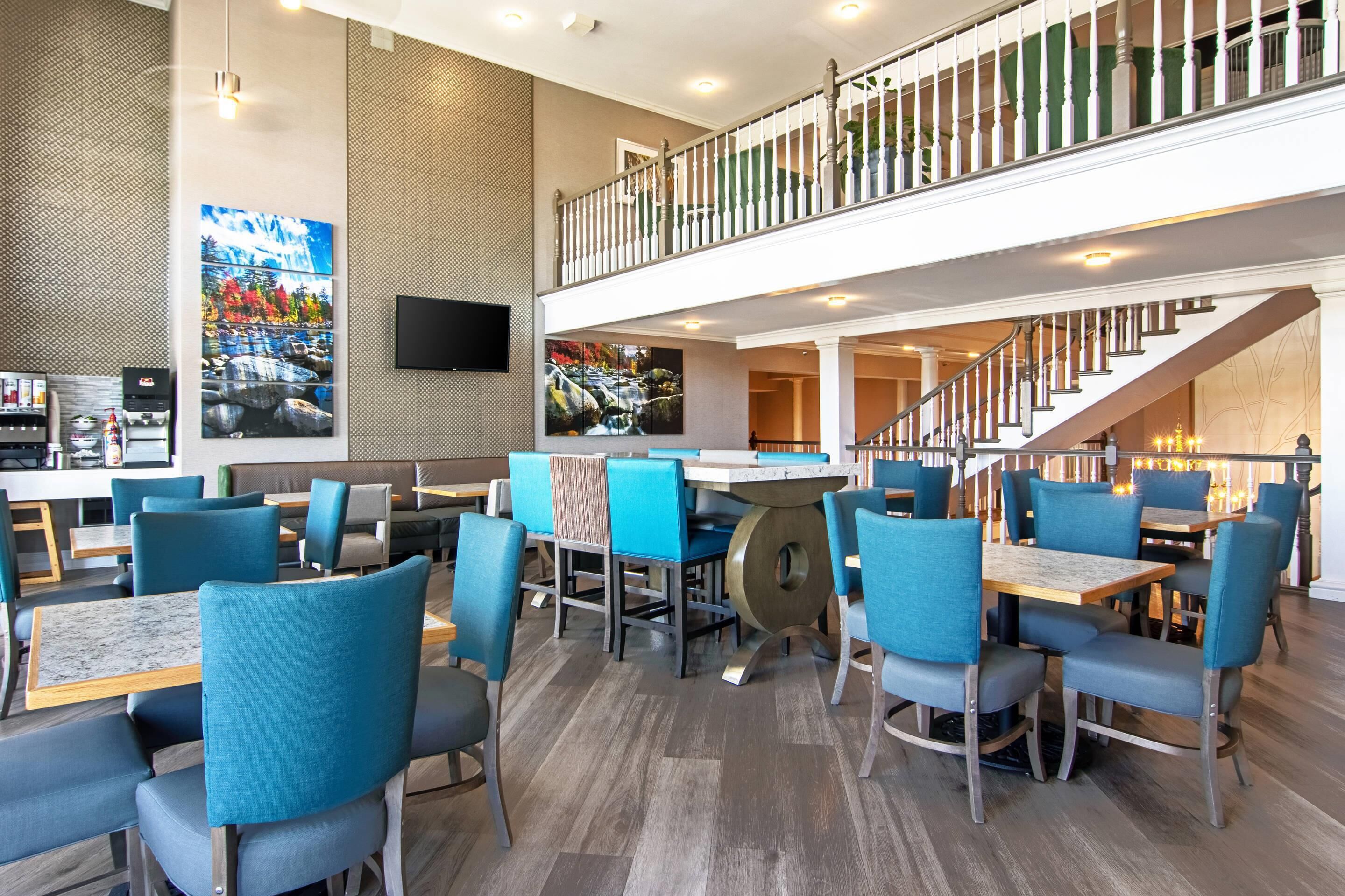 Un restaurante moderno con sillas azules, una mesa de madera y una escalera que lleva a un nivel superior.
