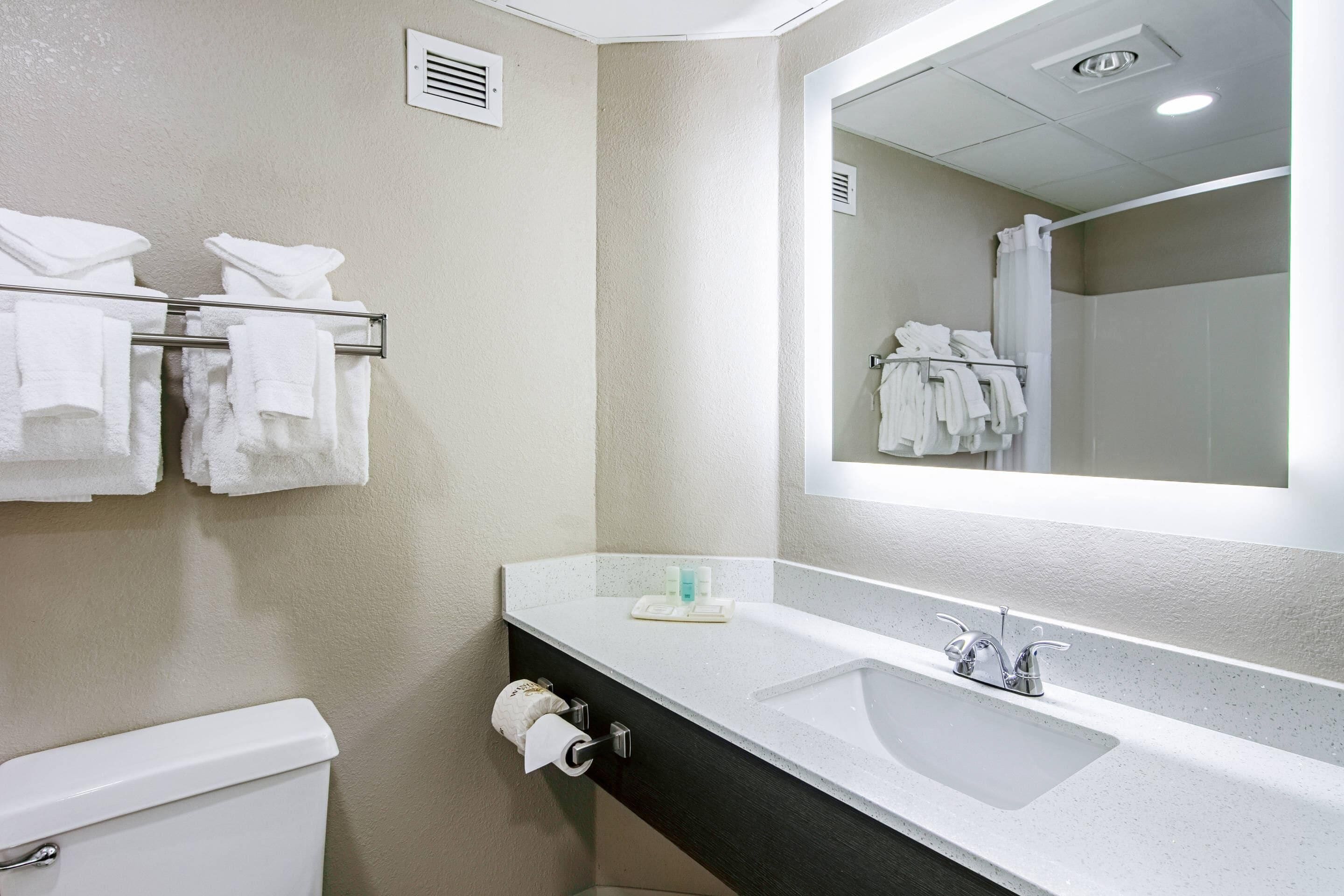 Un baño con un lavamanos blanco, un espejo y un perchero con varias toallas.