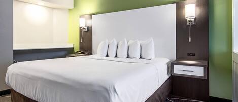 Ein Hotelzimmer mit einem großen Bett, einem Nachttisch, einer Wandlampe und einem Beistelltisch.
