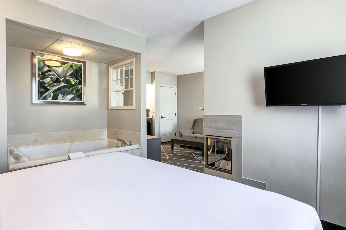 Une chambre d’hôtel dotée d’un grand lit, d’un téléviseur à écran plat fixé au mur, d’une salle de bain avec baignoire et d’une cheminée.