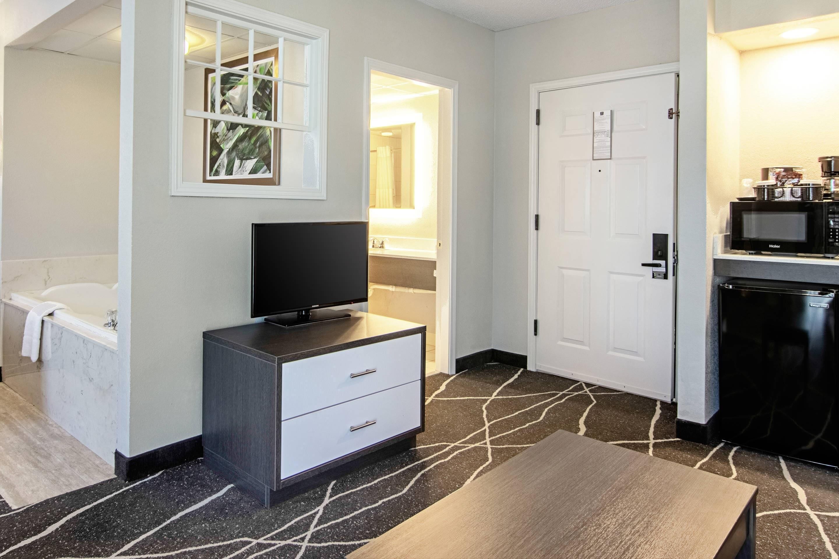 A hotel room with a flat-screen TV, a white dresser, a black coffee machine, and a microwave.