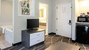 Habitación de hotel con televisor de pantalla plana, cómoda blanca, máquina de café negra y microondas.