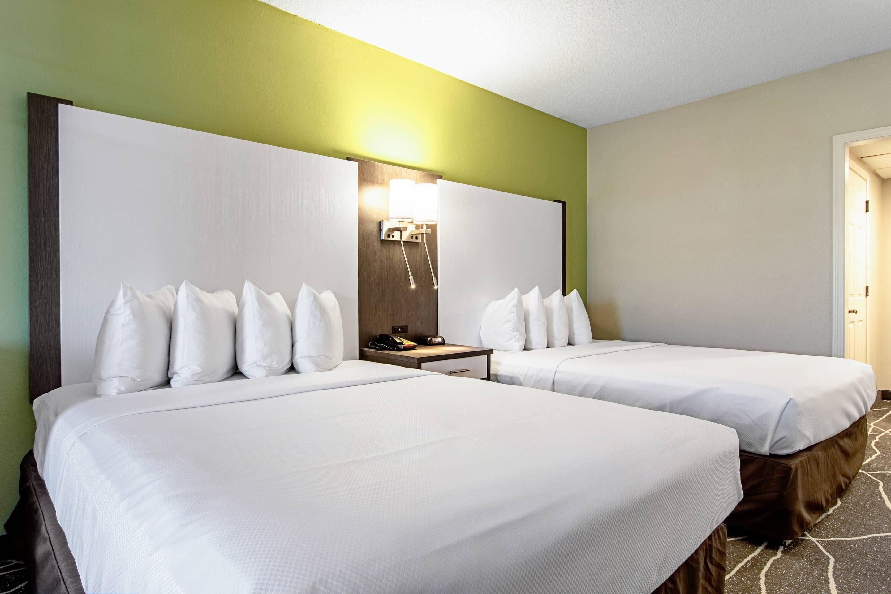 A hotel room with two beds, a nightstand, and a wall-mounted light fixture.