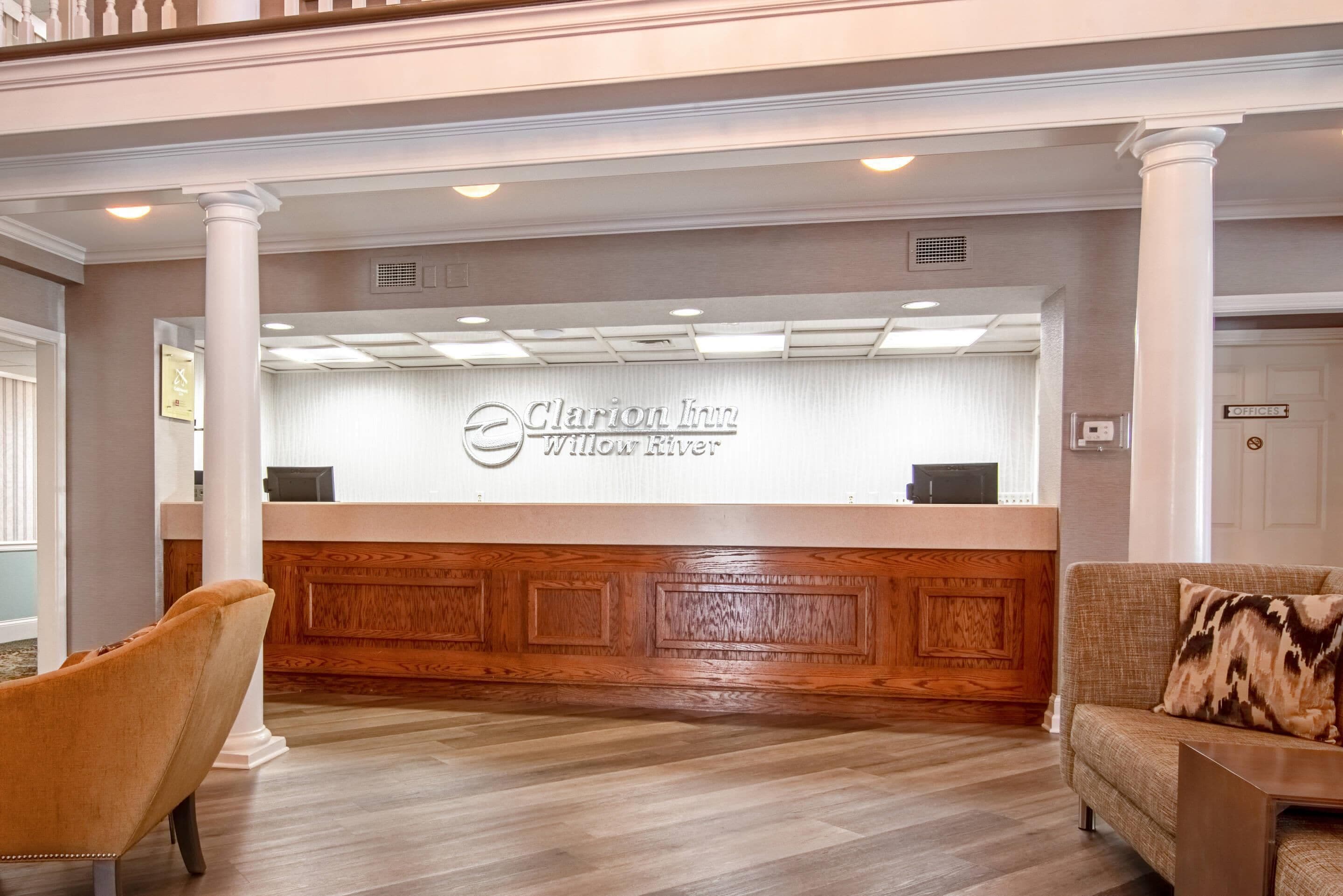 A reception area with a wooden reception desk, a plush armchair, and a sofa with a patterned pillow.