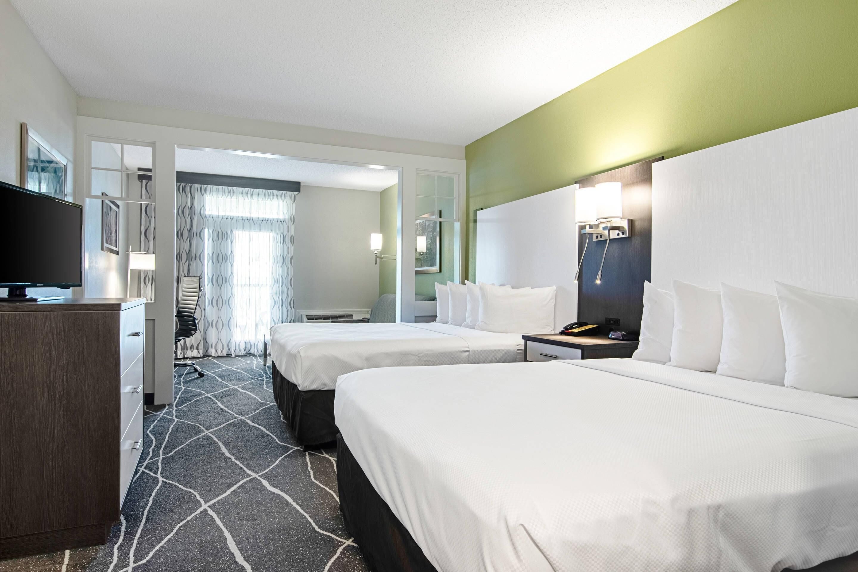 A hotel room with two beds, a desk, a television, and a bathroom visible through an open door.