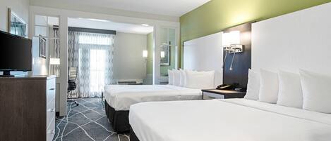 A hotel room with two beds, a desk, a television, and a bathroom visible through an open door.