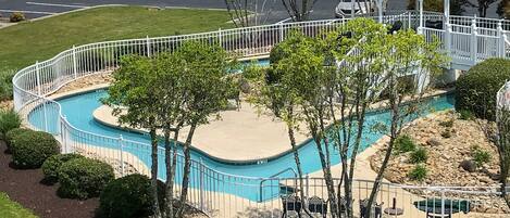 A swimming pool with a white fence, surrounded by trees and a gazebo.