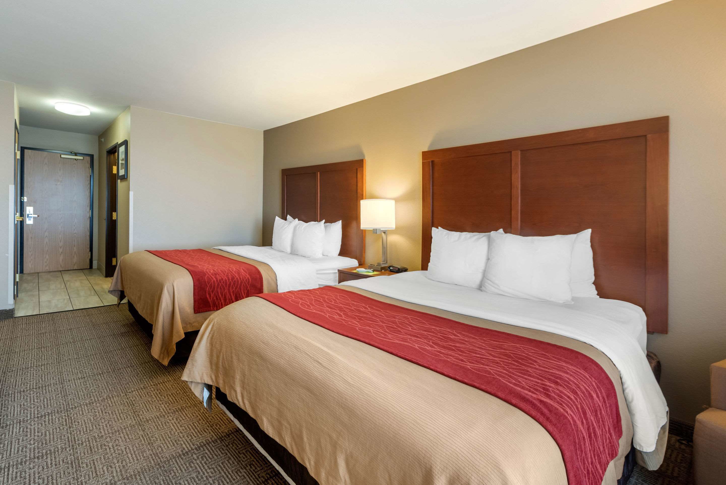 A hotel room with two beds, each with a wooden headboard, a red and beige bedspread, and a bedside lamp.