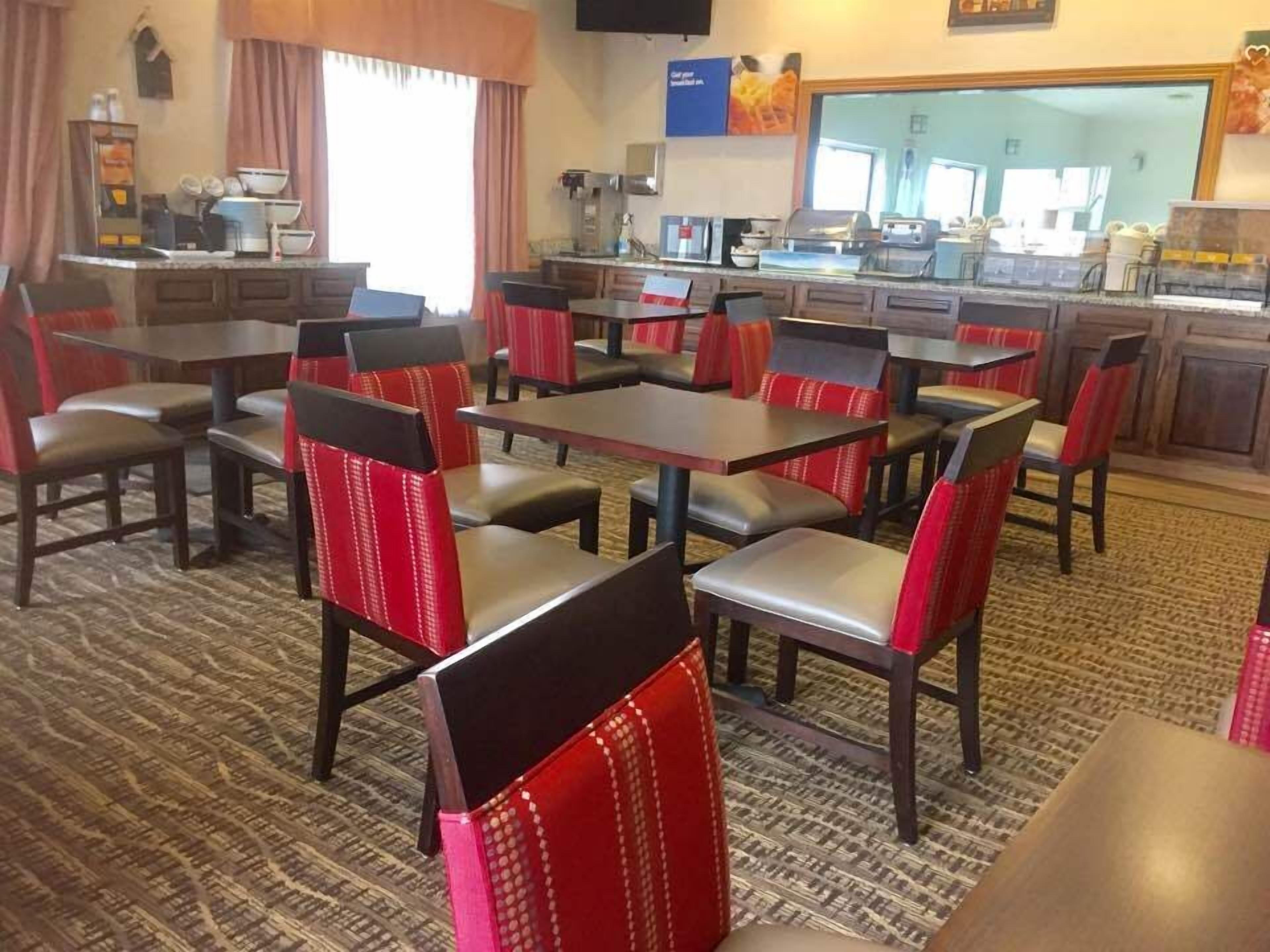 A restaurant with booths and tables, a kitchen area, and a large window with curtains.