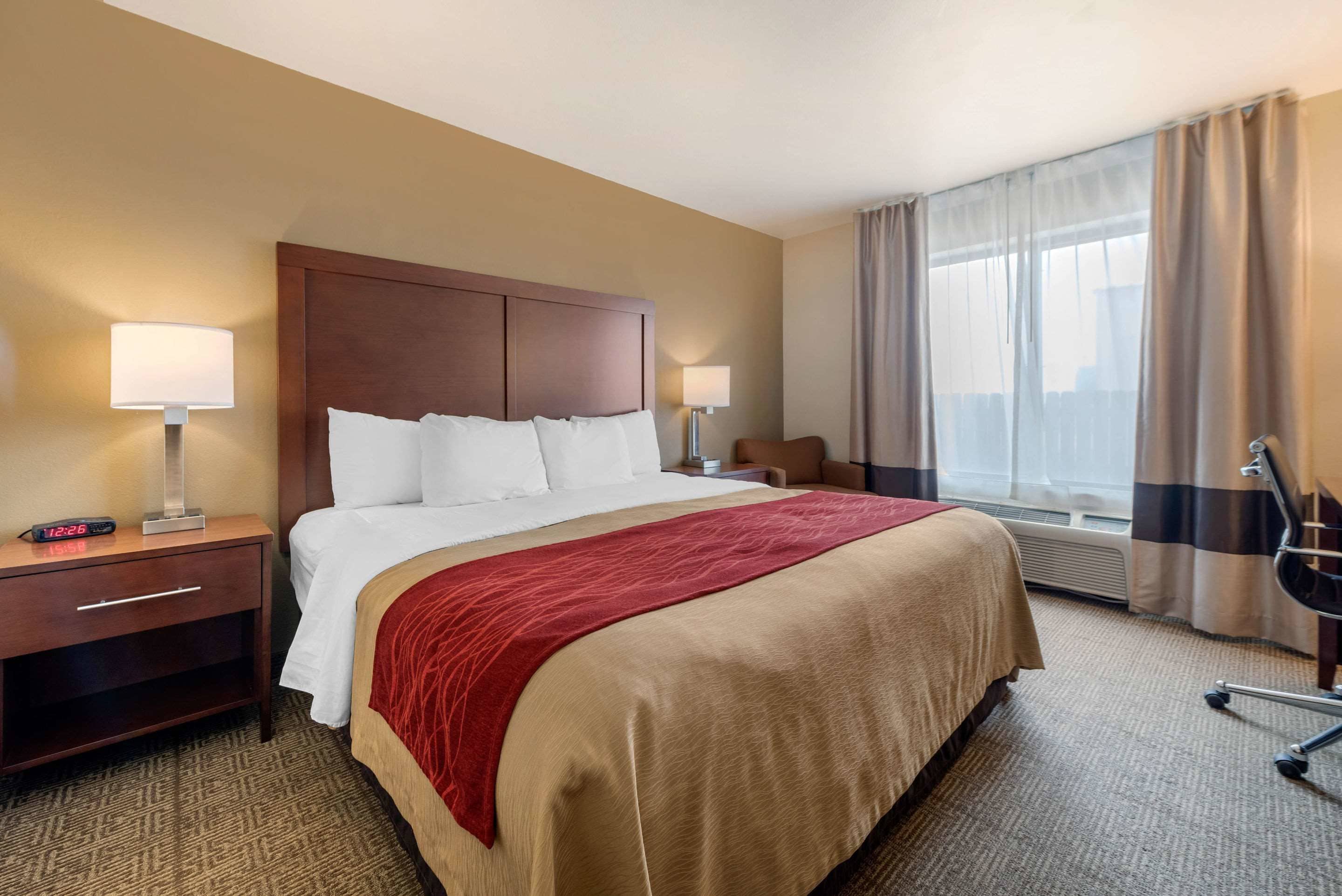 Habitación de hotel con una cama grande, dos mesitas de noche con lámparas, una silla y una ventana con cortinas.