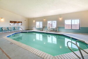 Una piscina interior con agua cristalina, rodeada de sillas y un solárium con baldosas.