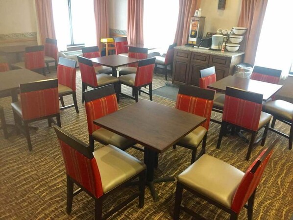 Un comedor de hotel con varias mesas y sillas, una zona de cocina al fondo y una alfombra estampada.