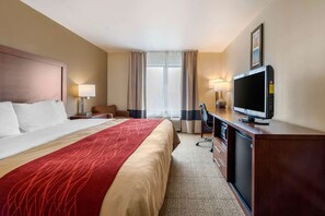 A hotel room with a large bed, a desk with a television, a chair, and a desk lamp.