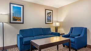 A hotel room with a blue sofa, a matching armchair, a wooden coffee table, and two framed pictures on the wall. - Comfort Inn Limon (Limon)
