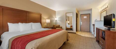 A hotel room with a large bed, a television, a desk with a lamp, and a mirror.