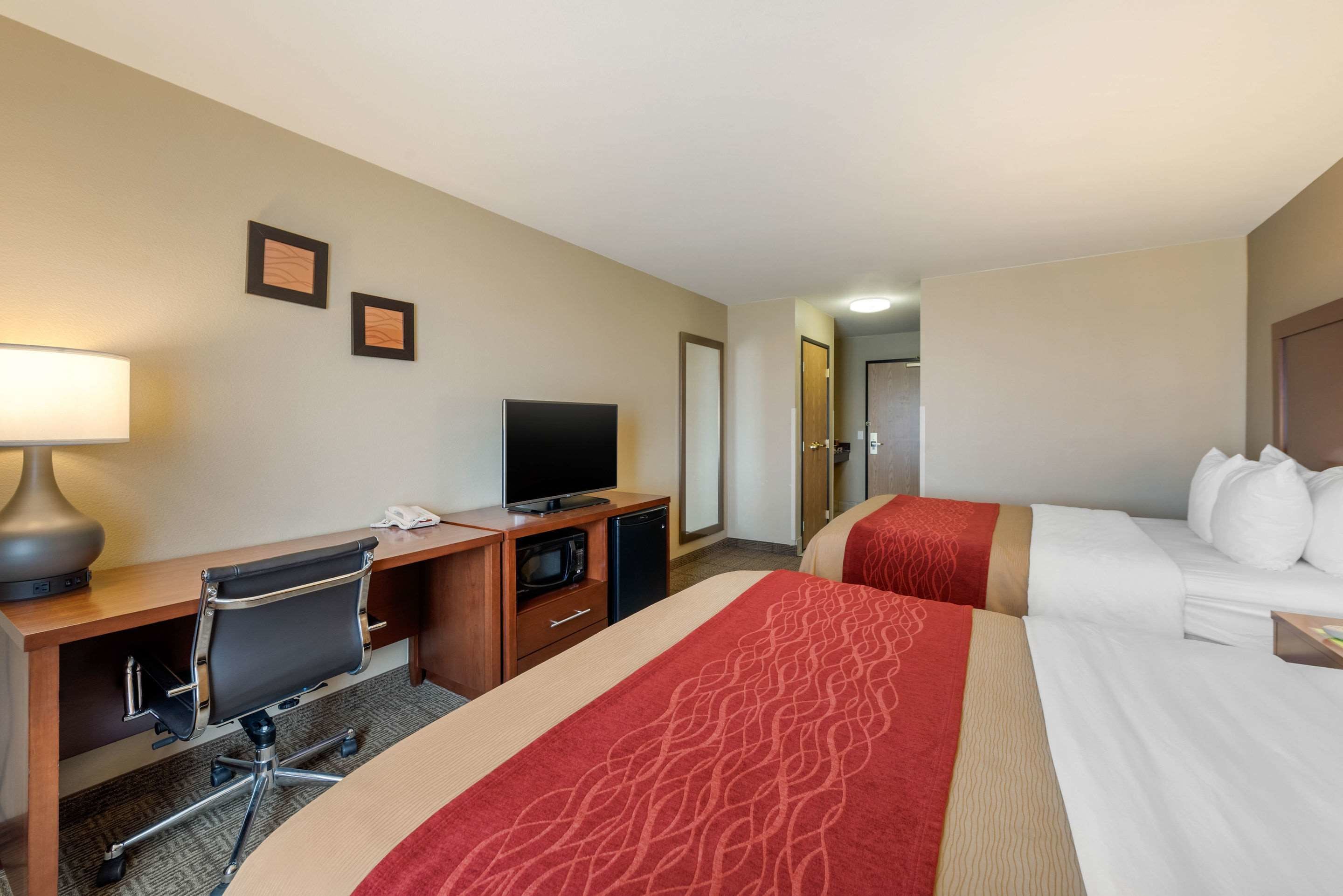 A hotel room with a bed, a desk with a computer, a television, and a lamp.
