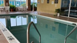 An indoor swimming pool with clear water, a tiled floor, and a few lounge chairs and potted plants around the pool area.