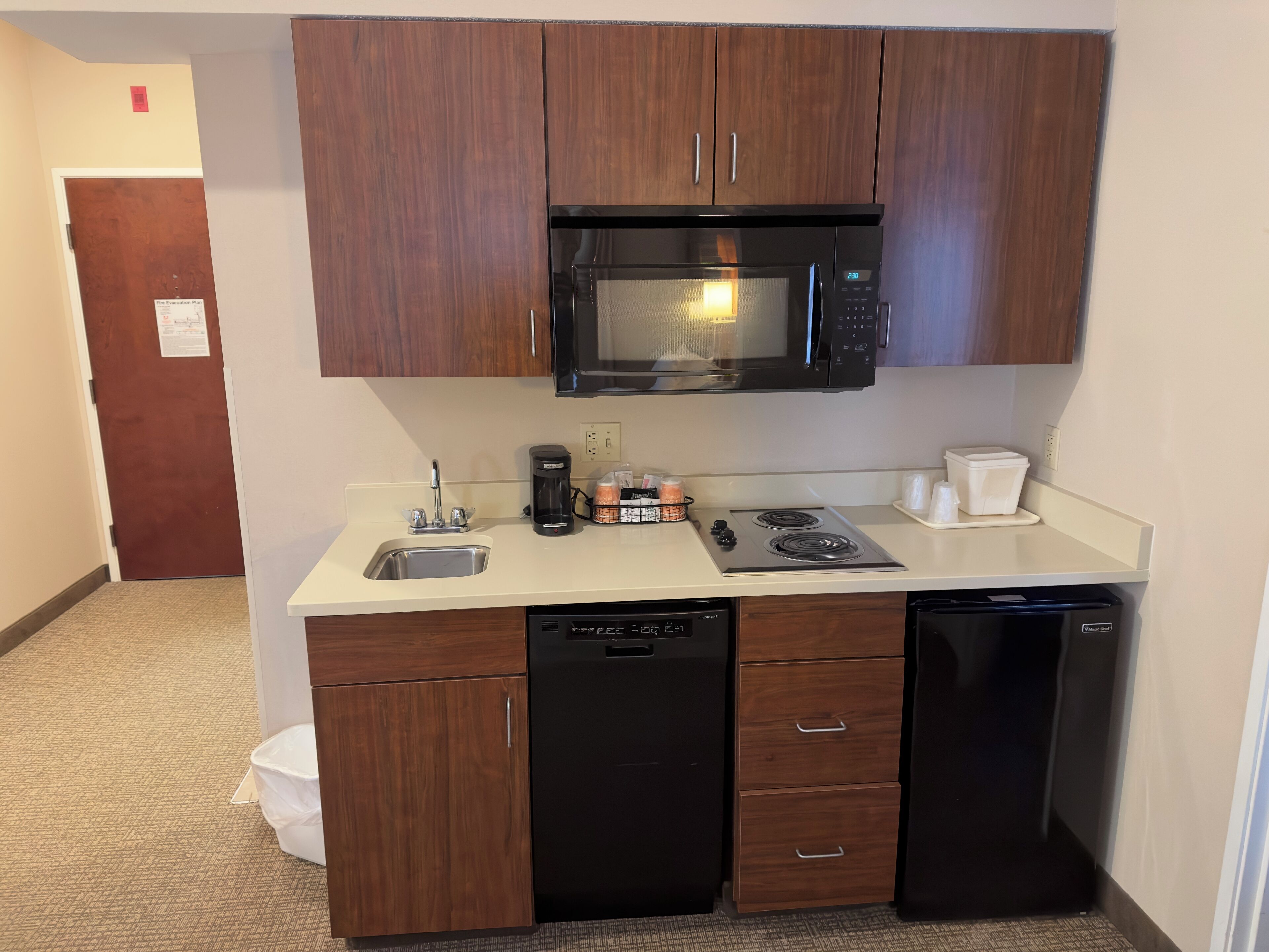 Una kitchenette compacta con microondas, cafetera y lavavajillas.