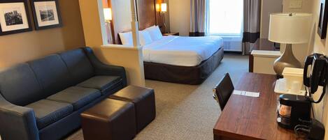 Una habitación de hotel con cama, sofá, cafetera y cuadros en la pared.