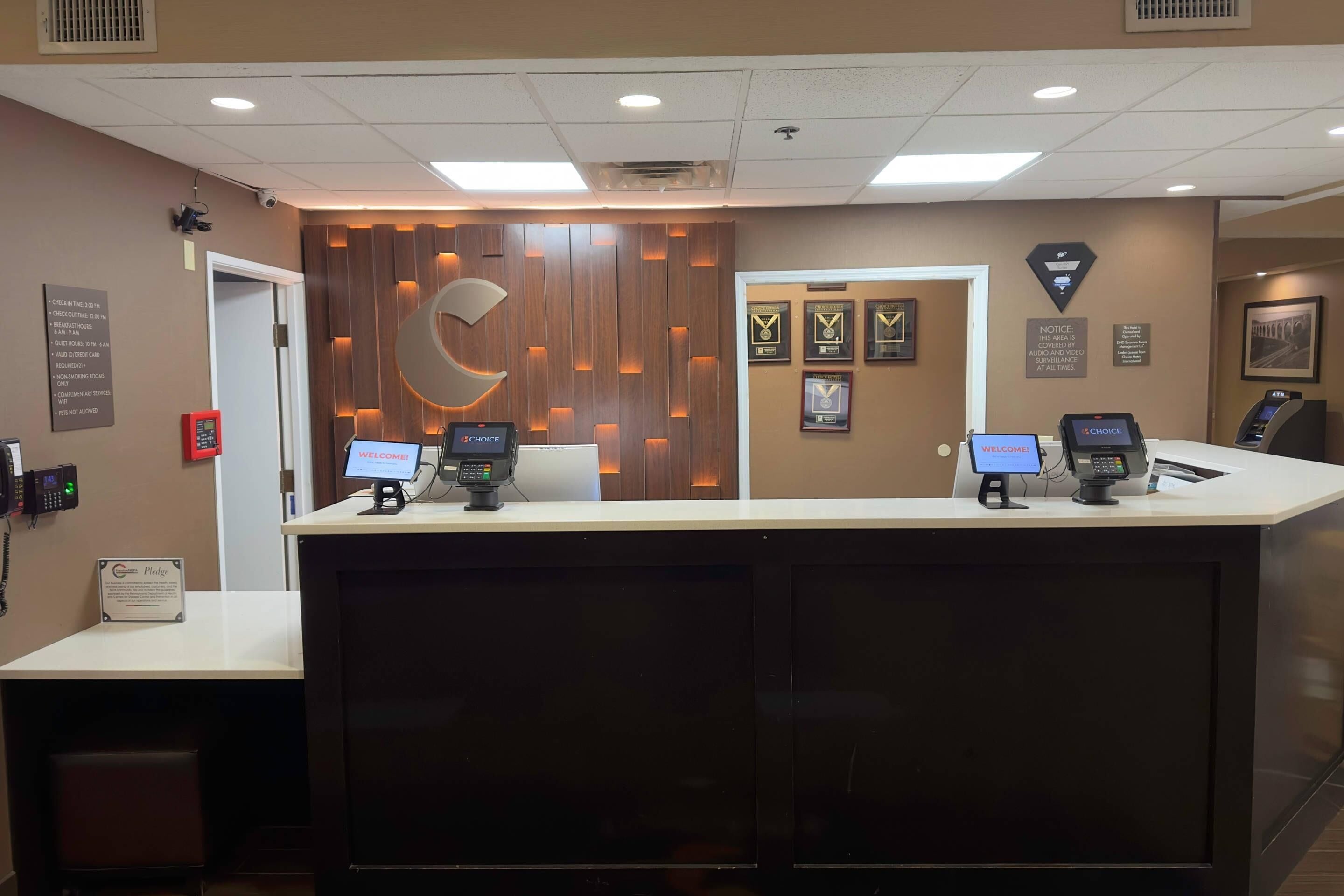 A reception desk with two computer monitors, a logo, and framed awards on the wall.