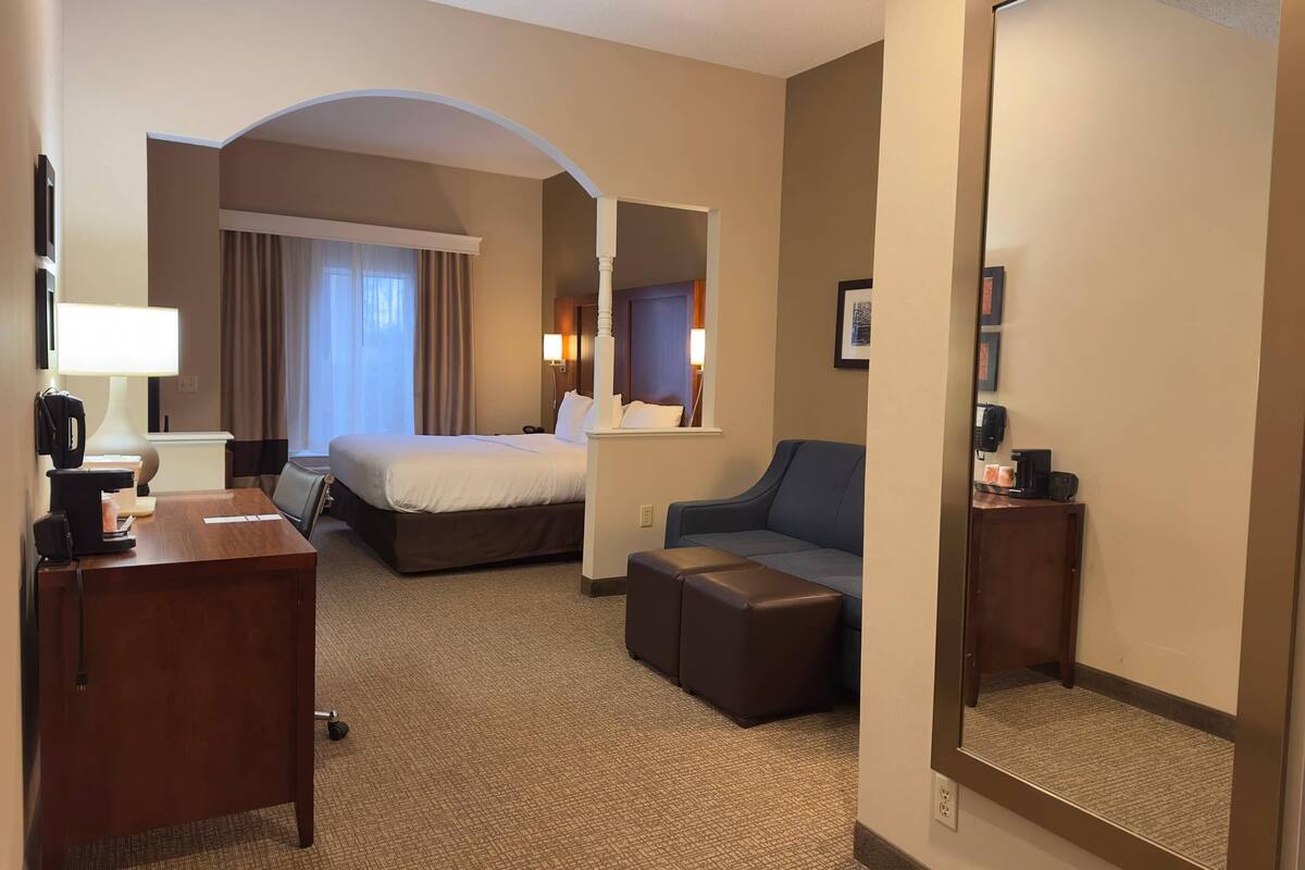 A hotel room with a bed, desk, chair, and a large mirror.