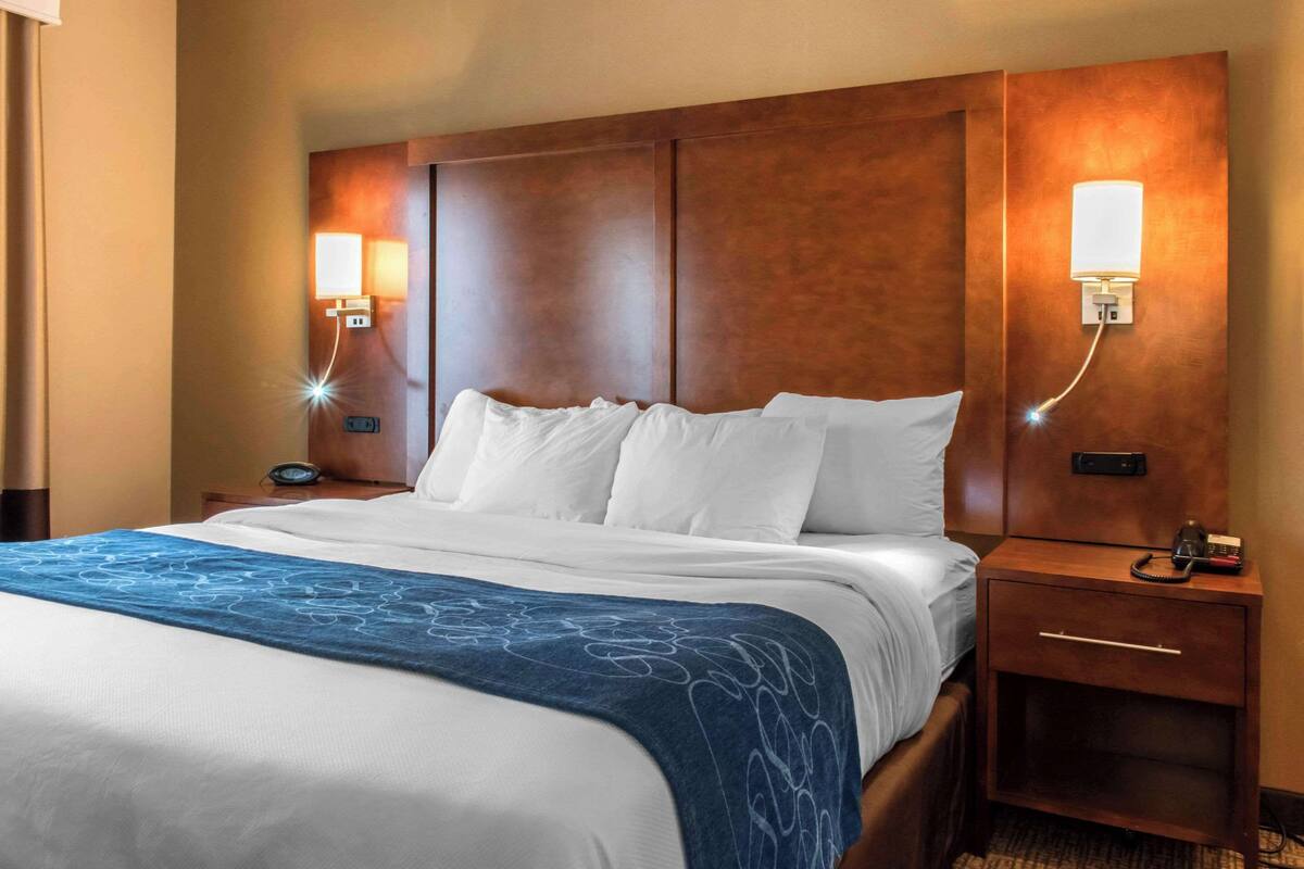 A hotel room with a large bed, two bedside tables, a nightstand, and wall-mounted lights.