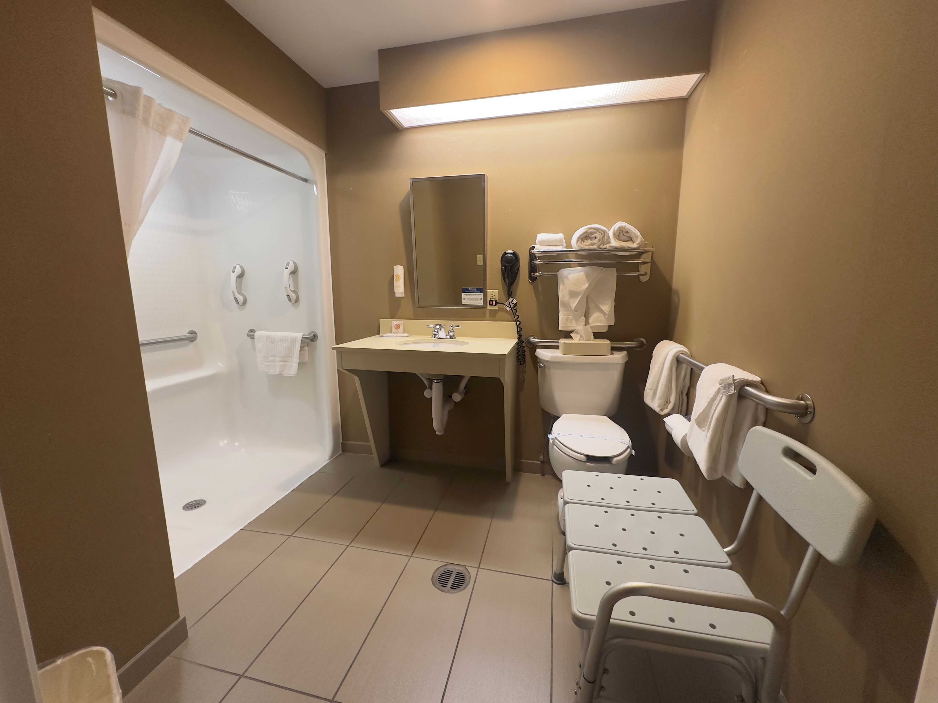 Un baño con bañera, lavamanos, inodoro y un banco accesible para sillas de ruedas.