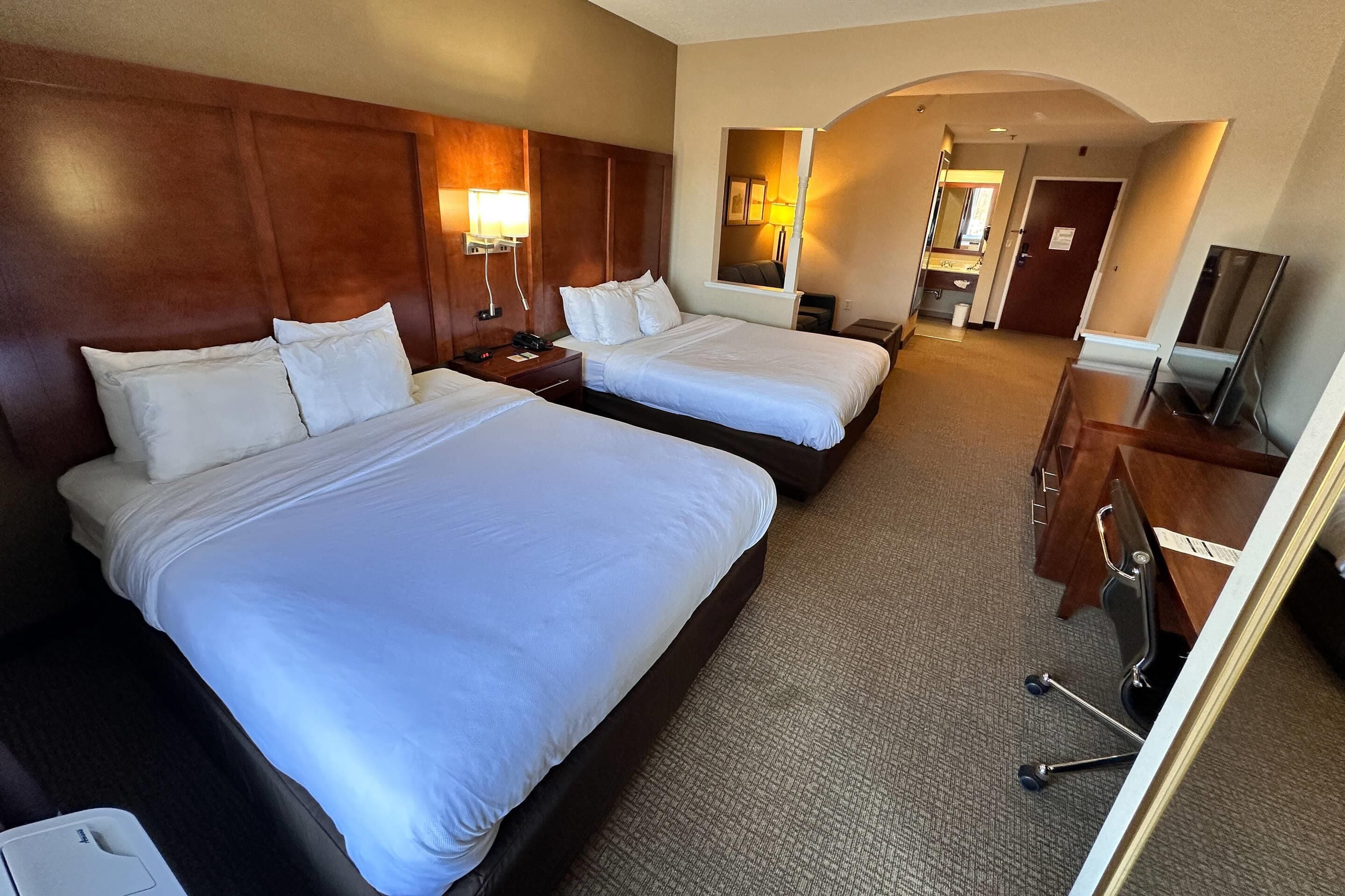 Habitación de hotel con dos camas, un escritorio con silla, televisor y espejo.