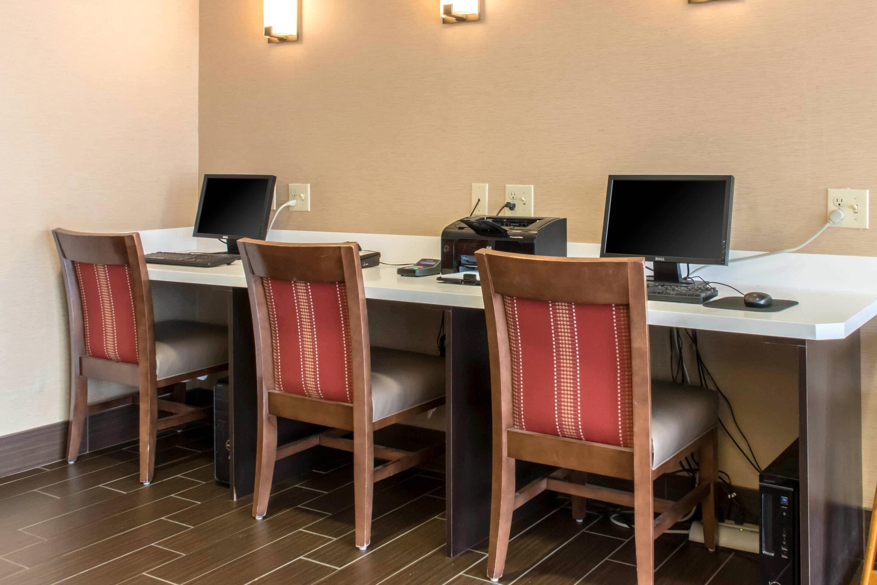 A hotel room with a desk, two computers, a printer, and four chairs.
