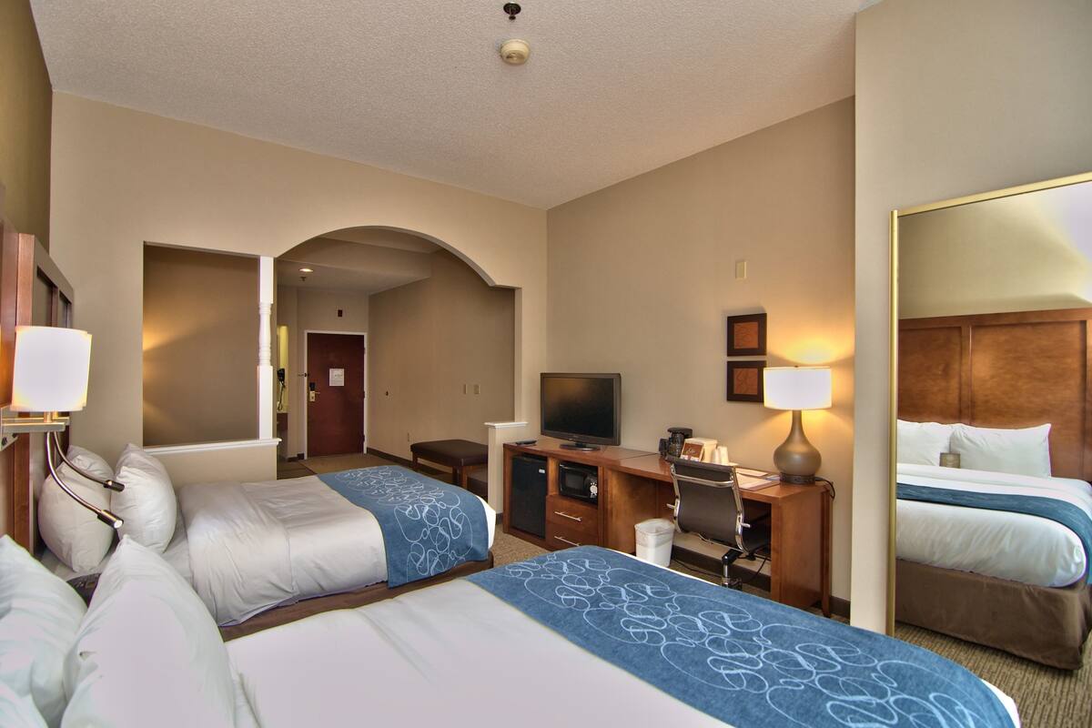 A hotel room with two beds, a desk, a television, and a mirror.
