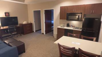 A compact hotel room with a kitchenette, a dining area with a table and chairs, a TV, and a sofa.