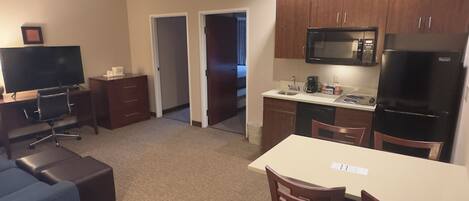 Una habitación de hotel compacta con kitchenette, zona de comedor y sala de estar con televisor y escritorio.
