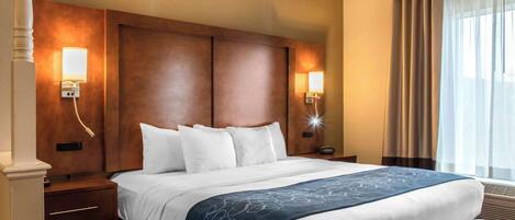 A hotel room with a large bed, two bedside lamps, a nightstand, and a window with curtains.