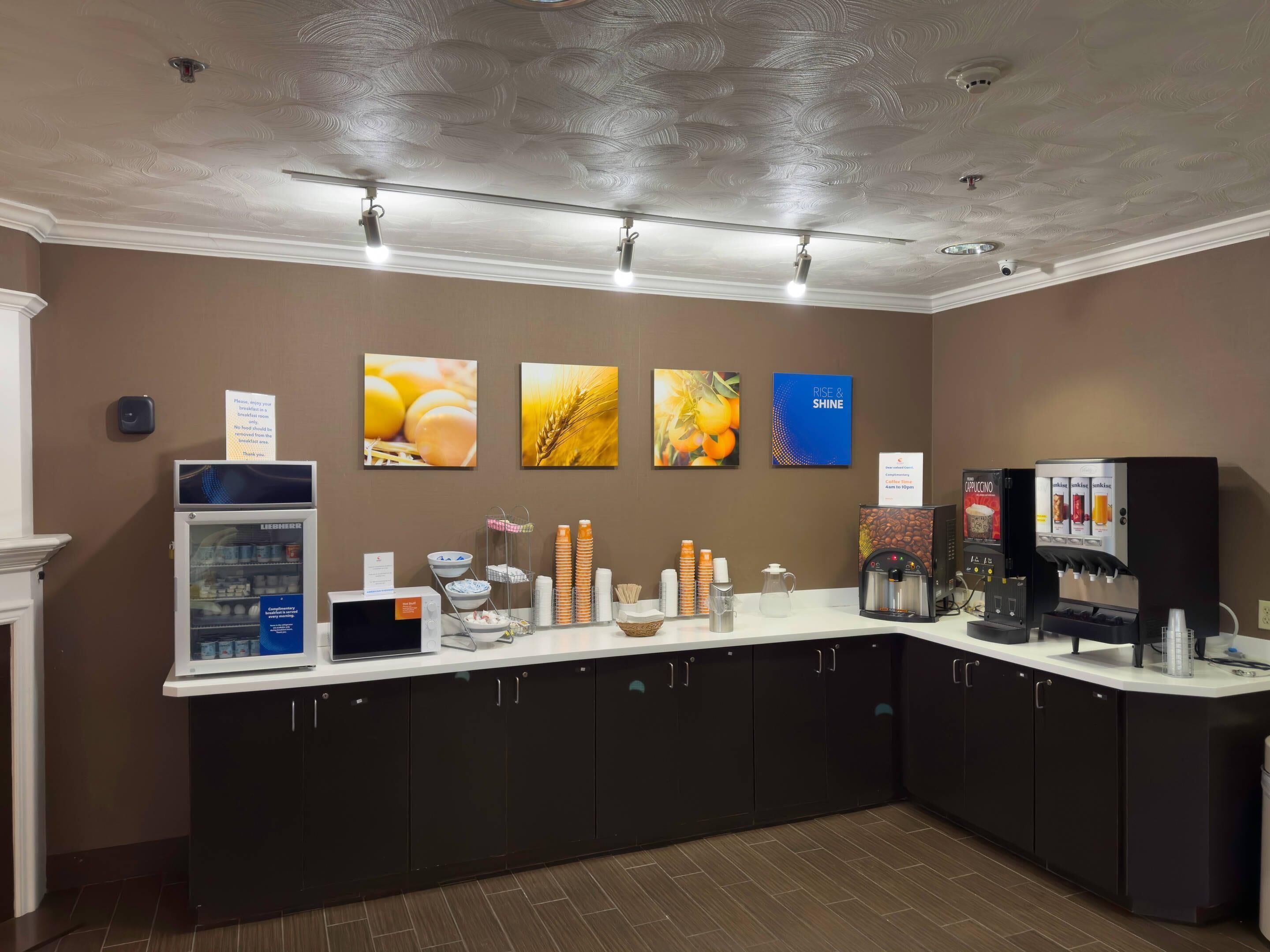 A breakfast bar with a refrigerator, coffee machines, and a sign indicating the coffee machine is open.