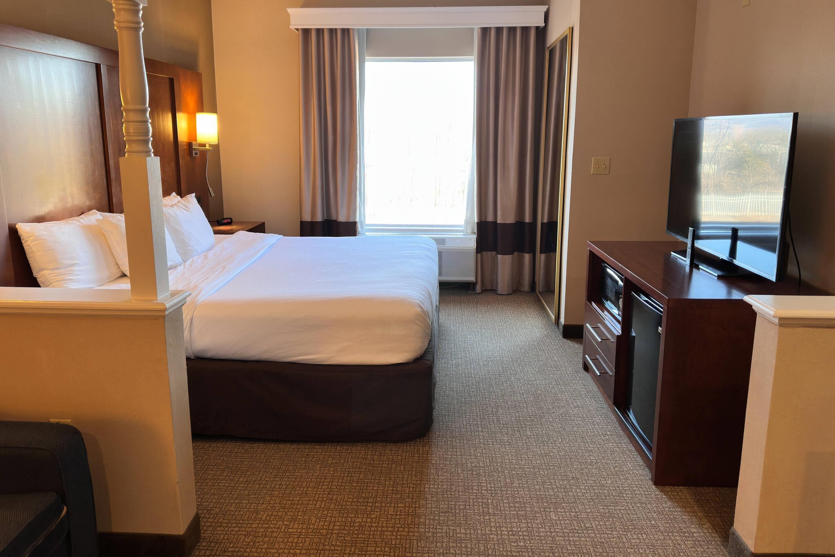 A hotel room with a bed, a desk, a television, and a window with curtains.