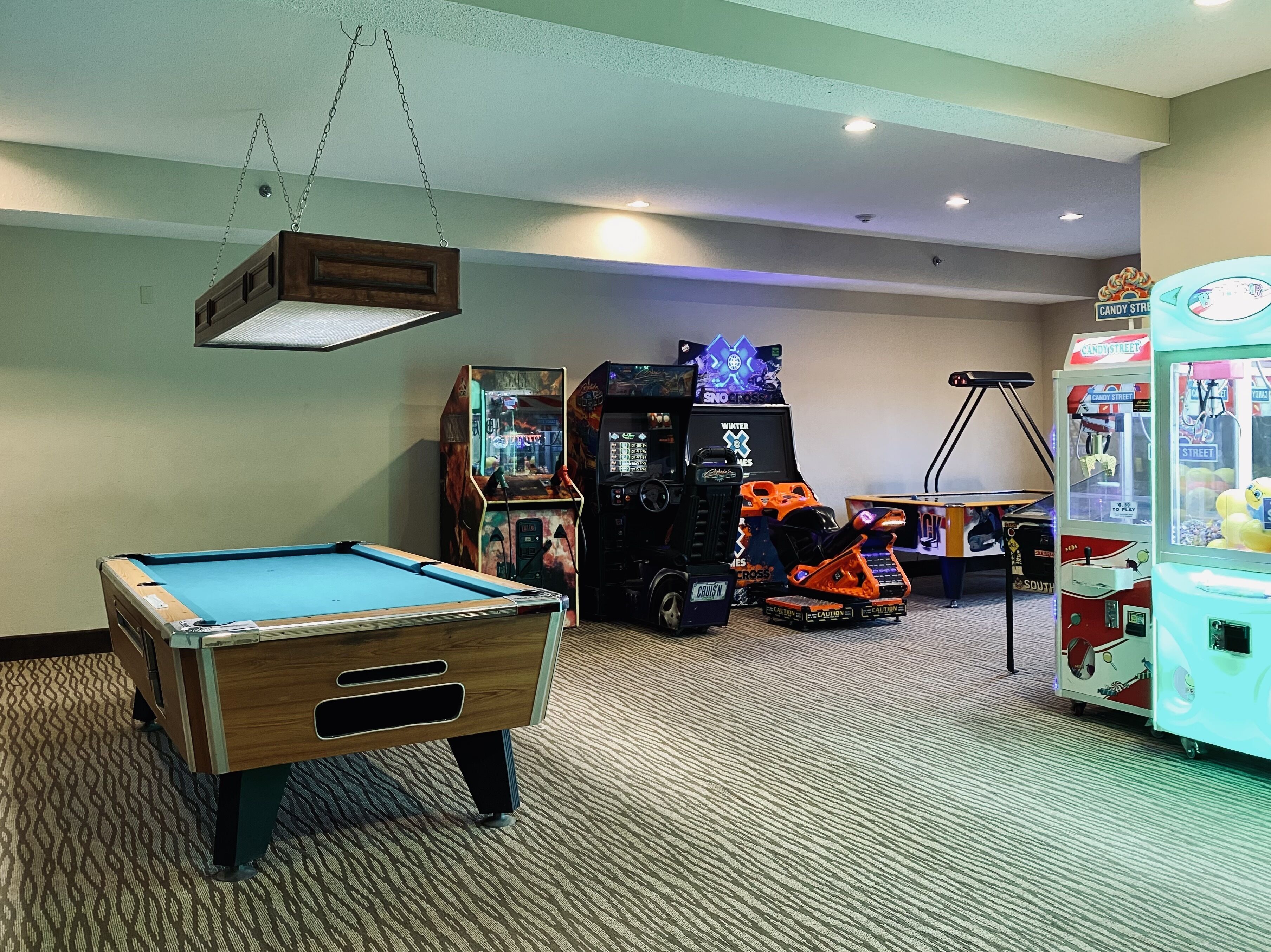 A pool table in a room with arcade games and a claw machine.