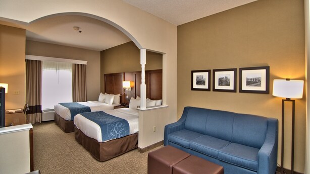 A hotel room with two beds, a blue sofa, a desk, and a mirror.