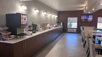 Una cocina moderna con una encimera larga, equipada con diferentes electrodomésticos y alimentos, además de un área de descanso con mesas y sillas.