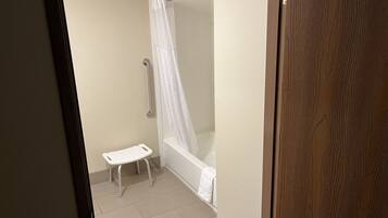 Une salle de bain avec une douche, une baignoire blanche et un petit tabouret blanc.