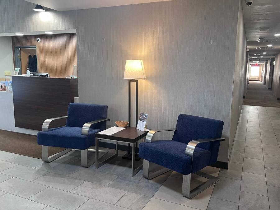 A hotel lobby with two blue armchairs, a small table, a floor lamp, and a reception desk.