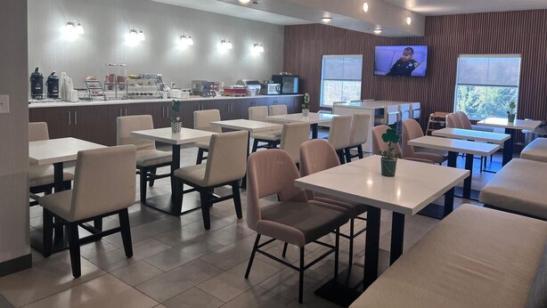 A modern dining area with multiple tables and chairs, a kitchen counter with appliances, and a television screen. - Wingate by Wyndham Clearfield (Clearfield)