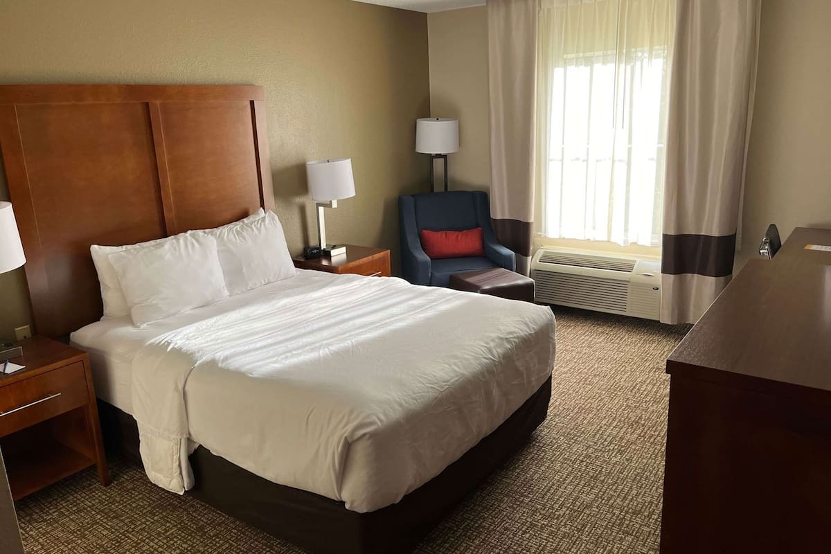 A hotel room with a large bed, a desk, a chair, a lamp, and a window with curtains.