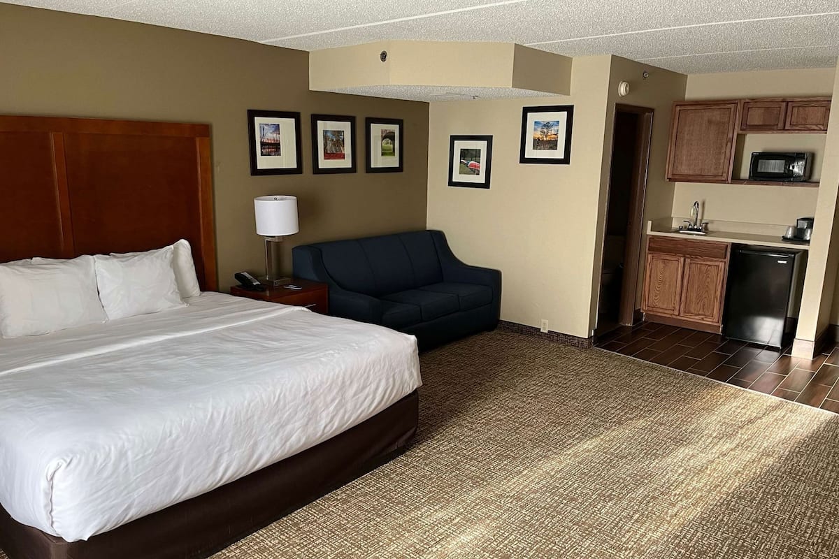 A hotel room with a bed, a desk, a chair, a microwave, and a refrigerator.
